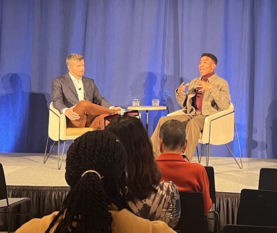 two men sitting on a stage in comfy chairs giving a fireside chat