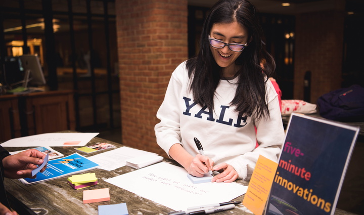 Student in Yale t-shirt writes ideas on paper during pop-up event