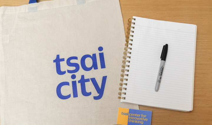 Flatlay image of notebook, pen, and Tsai CITY tote bag and sticker