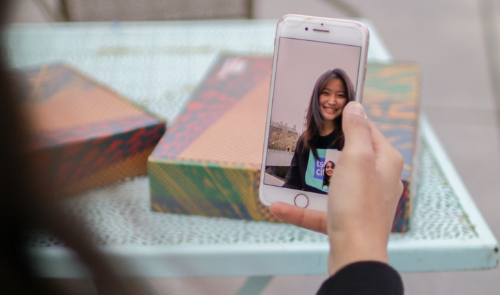 Arm holding phone, showing FaceTime call with student in Tsai CITY sweatshirt