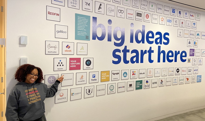 woman point at a wall with the words "big ideas start here" on it