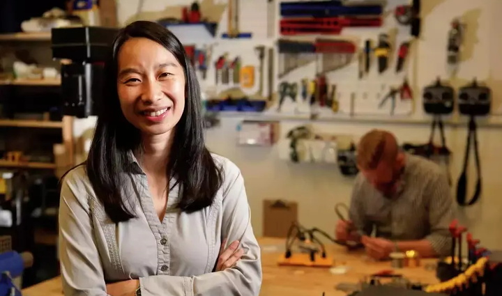 A woman poses in front of a workbench, surrounded by tools, showcasing her readiness for hands-on work.