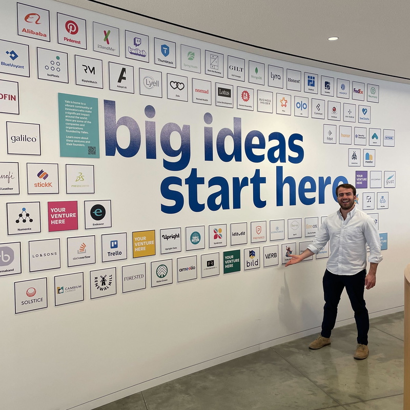 A man standing by a "Big Ideas Start Here" sign on a wall.