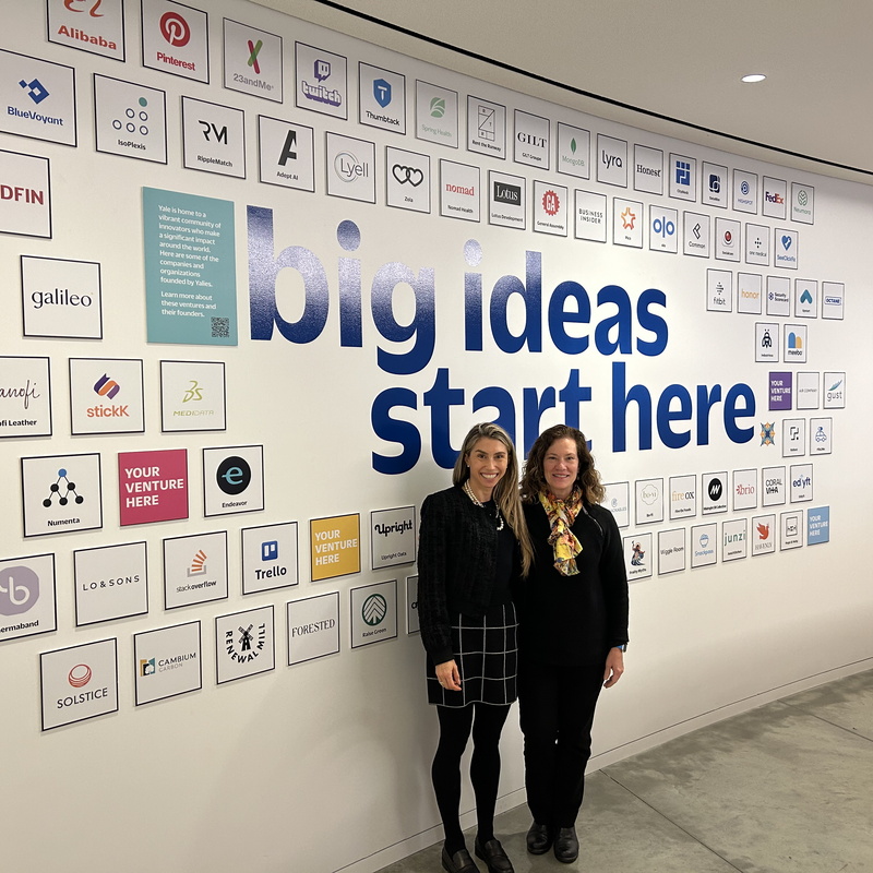 two people standing by a "Big Ideas Start Here" sign on a wall.