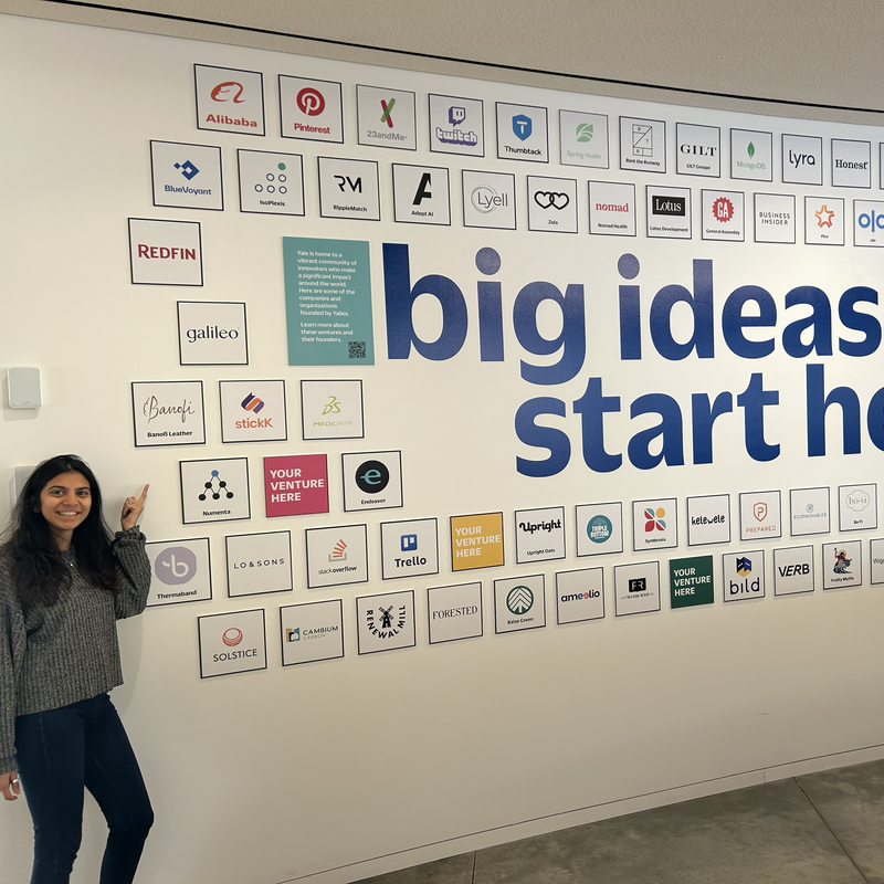 A woman standing by a "Big Ideas Start Here" sign on a wall.