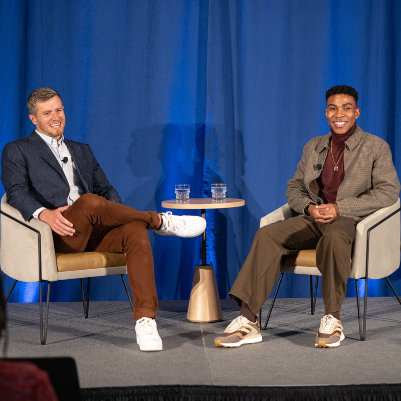 two individuals sitting in chairs on a stage with a small table between them