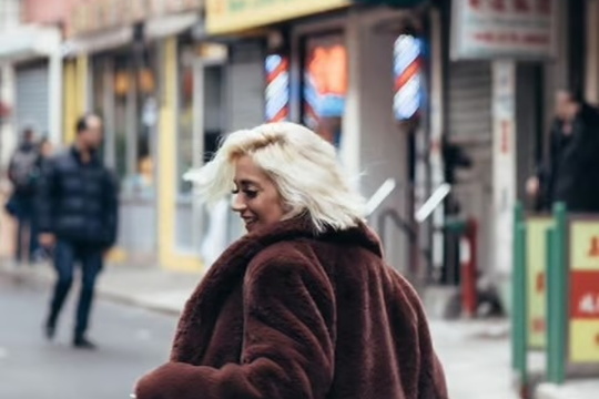 A fashionable woman in a fur coat walking through a cityscape.