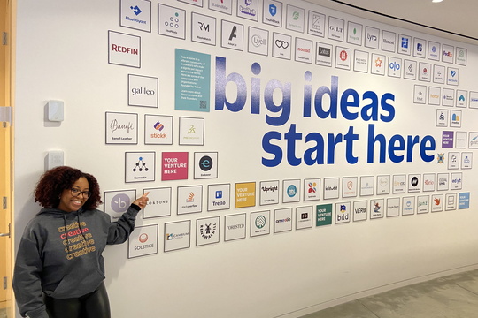 woman point at a wall with the words "big ideas start here" on it
