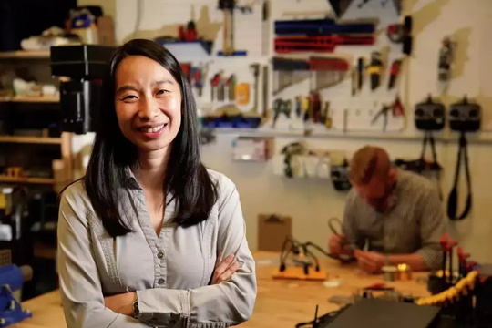 A woman poses in front of a workbench, surrounded by tools, showcasing her readiness for hands-on work.